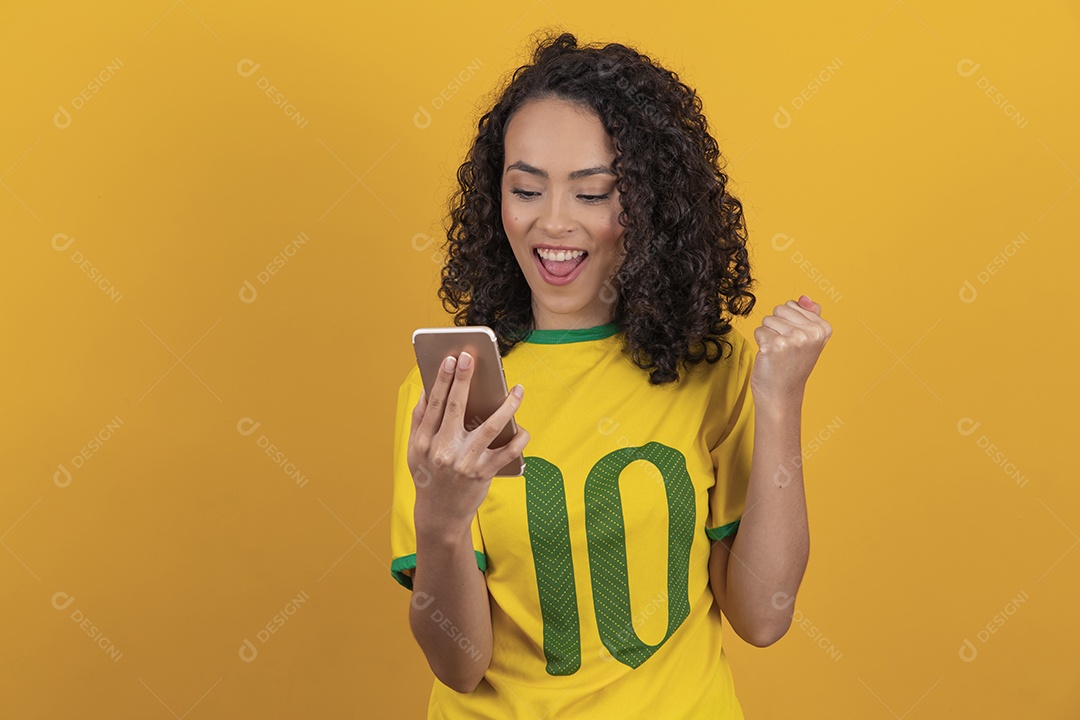 Mulher jovem usando camiseta da seleção brasileira futebol cabelo cacheado sobre fundo amarelo