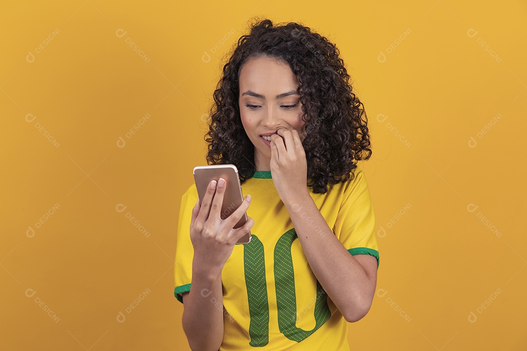 Mulher jovem usando camiseta da seleção brasileira futebol cabelo cacheado sobre fundo amarelo