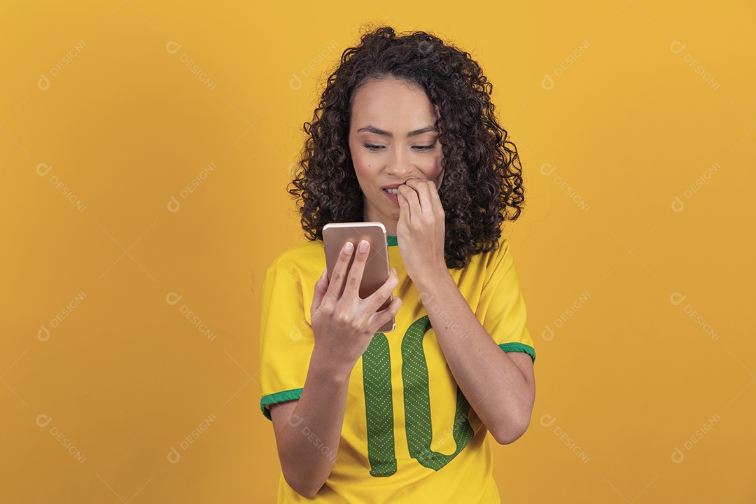 Mulher jovem usando camiseta da seleção brasileira futebol cabelo cacheado sobre fundo amarelo