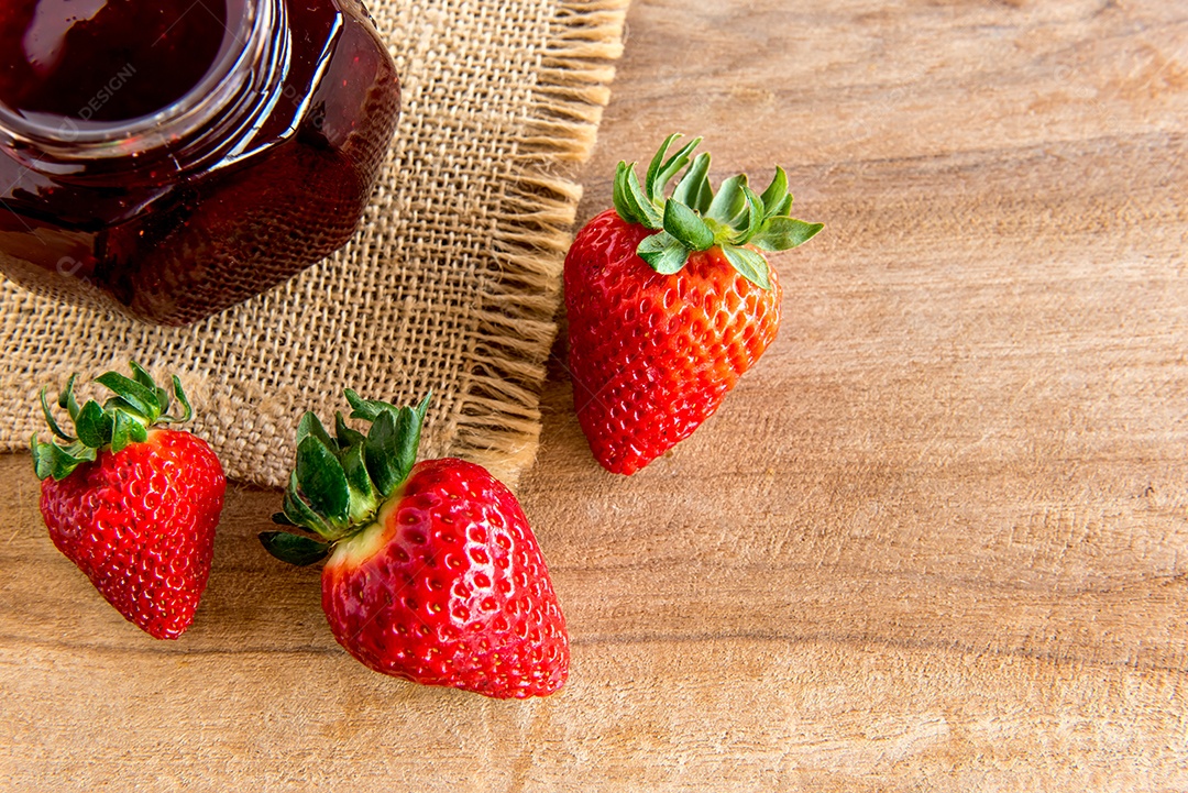 Geleia de morango e morangos na mesa de madeira.