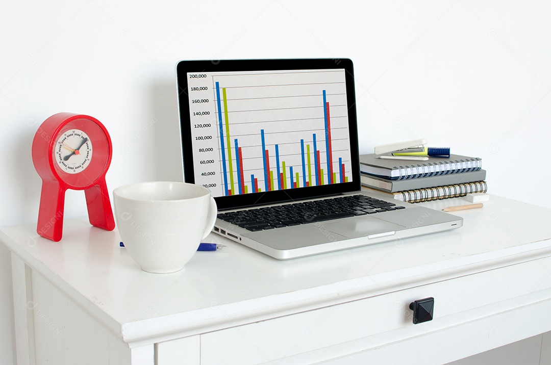 Laptop e relógio e copo e livro na mesa.