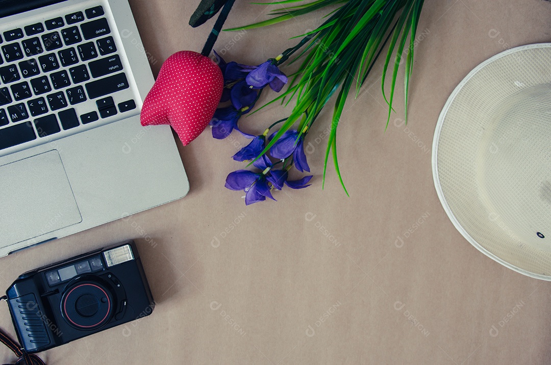 Câmera de flores e chapéu com laptop em fundo marrom.