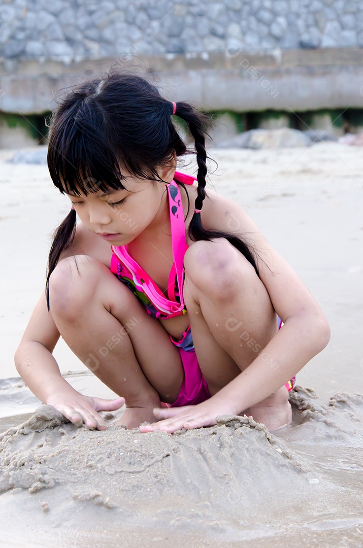 Garota brincando na areia da praia.