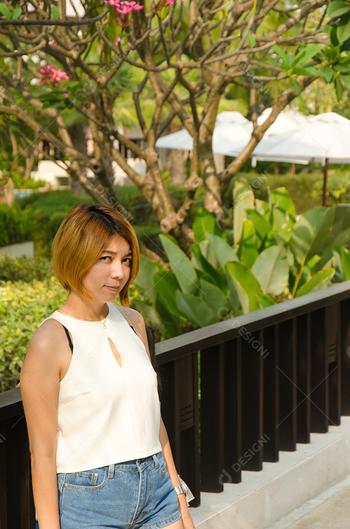 Mulher asiática vestindo camisa branca em pé no jardim.