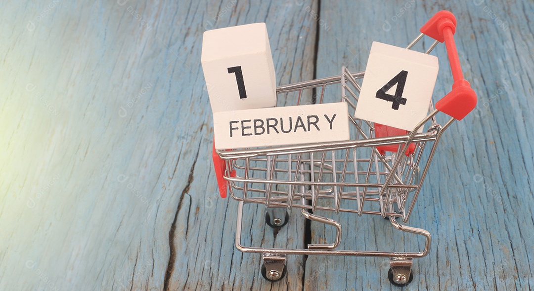 Carrinho de supermercado pequeno com calendário de madeira dia 14 de fevereiro em fundo de madeira.