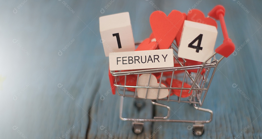 Carrinho de supermercado pequeno cheio de corações de dia dos namorados com calendário de madeira dia 14 de fevereiro em um fundo desfocado.