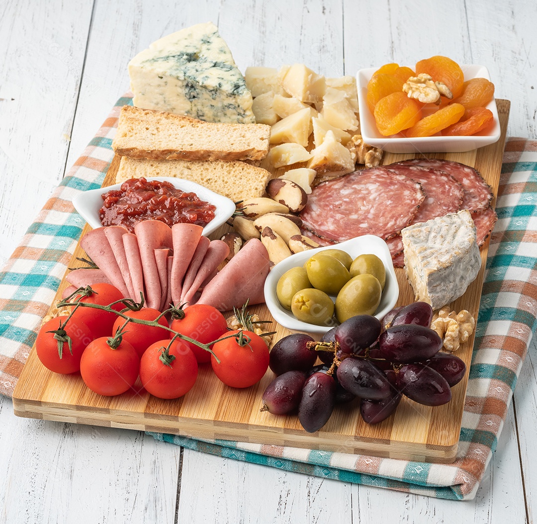 Tábua de aperitivos com queijo, nozes, frutas, torradas e charcutaria sobre a mesa de madeira.