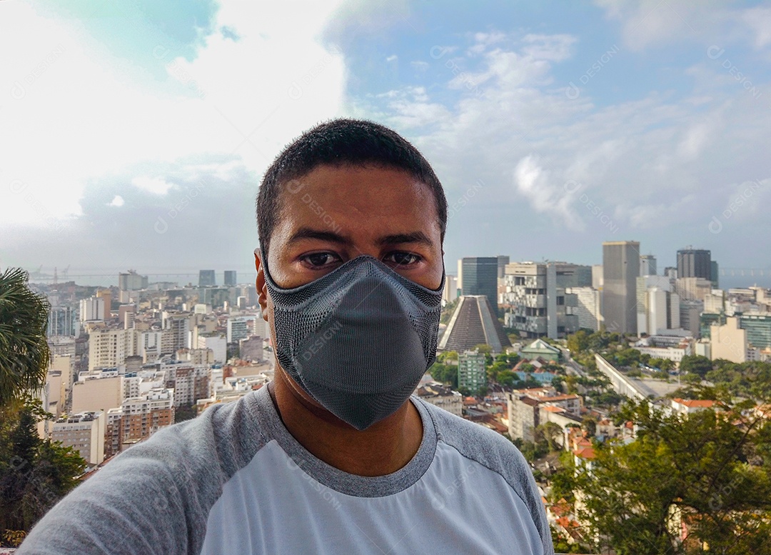 Homem negro usando máscara com o centro do Rio de Janeiro ao fundo, durante a pandemia de coronavírus no Brasil.