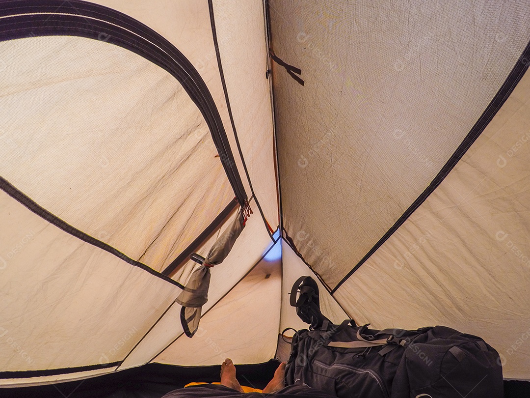 homem deitado dentro de uma barraca de acampamento fechada.