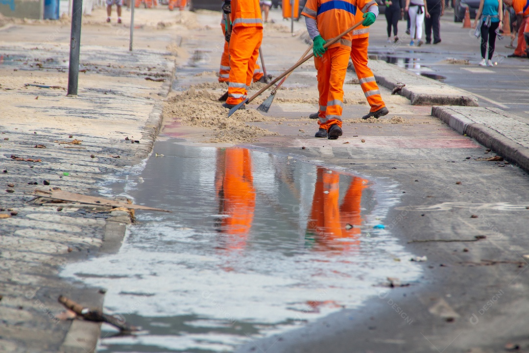 trabalhadores de limpeza removendo areia do calçadão da praia do Leblon, no Rio de Janeiro, Brasil