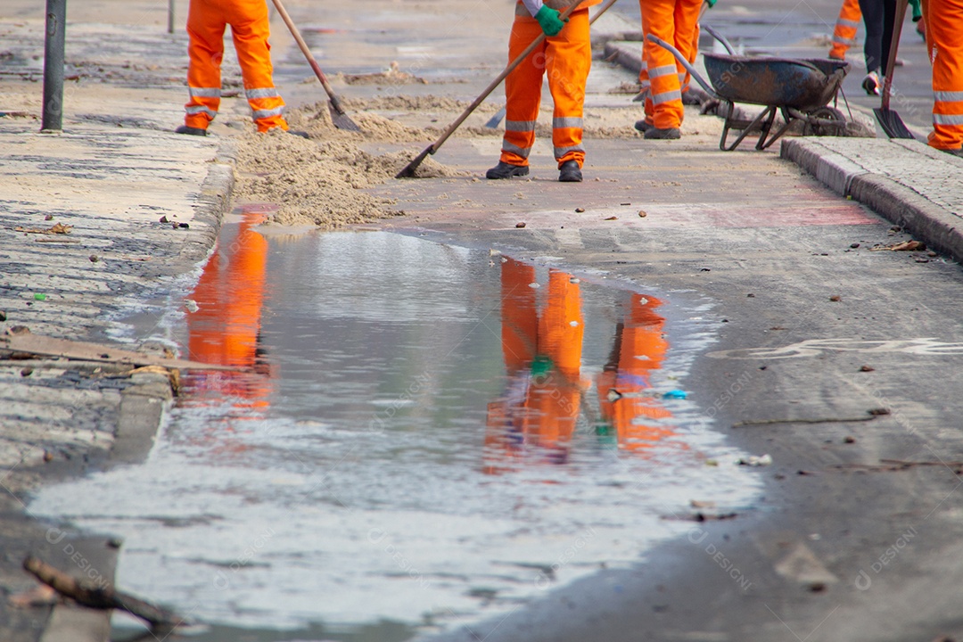 trabalhadores de limpeza removendo areia do calçadão da praia do Leblon, no Rio de Janeiro, Brasil