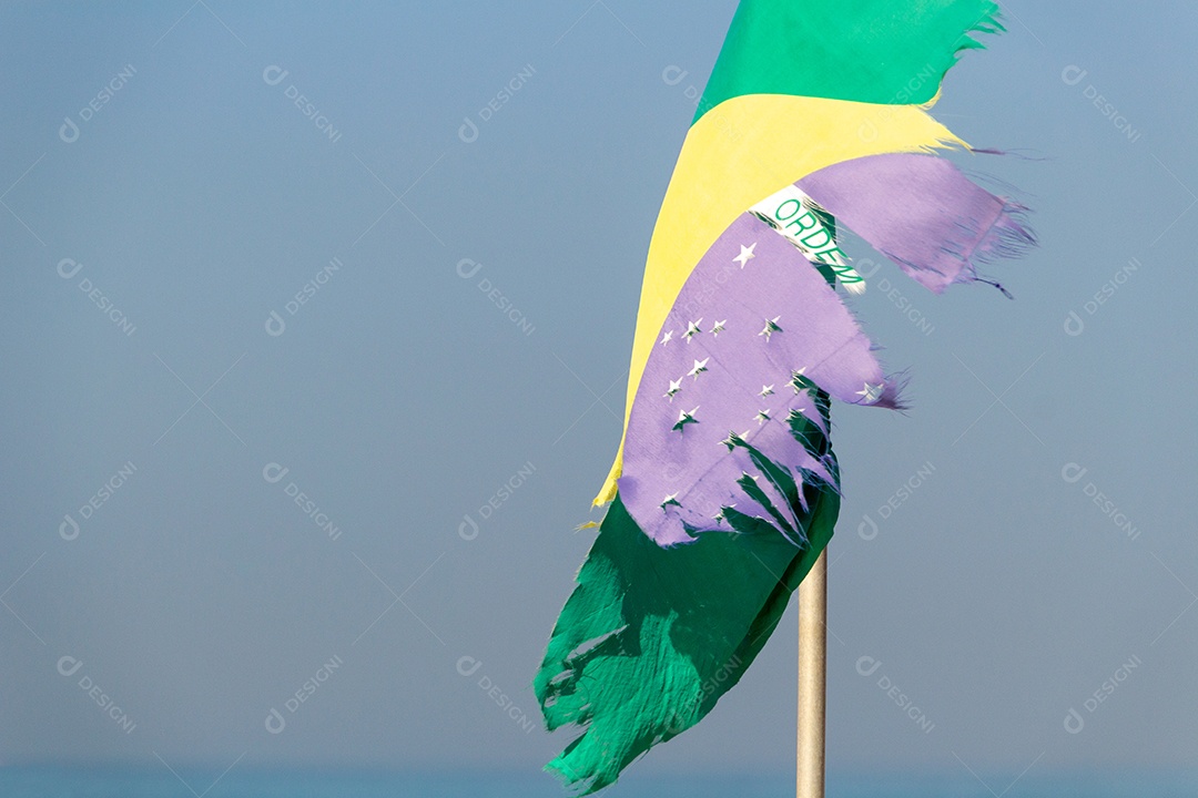 Bandeira do Brasil desbotada e rasgada ao ar livre na praia de Copacabana, no Rio de Janeiro.