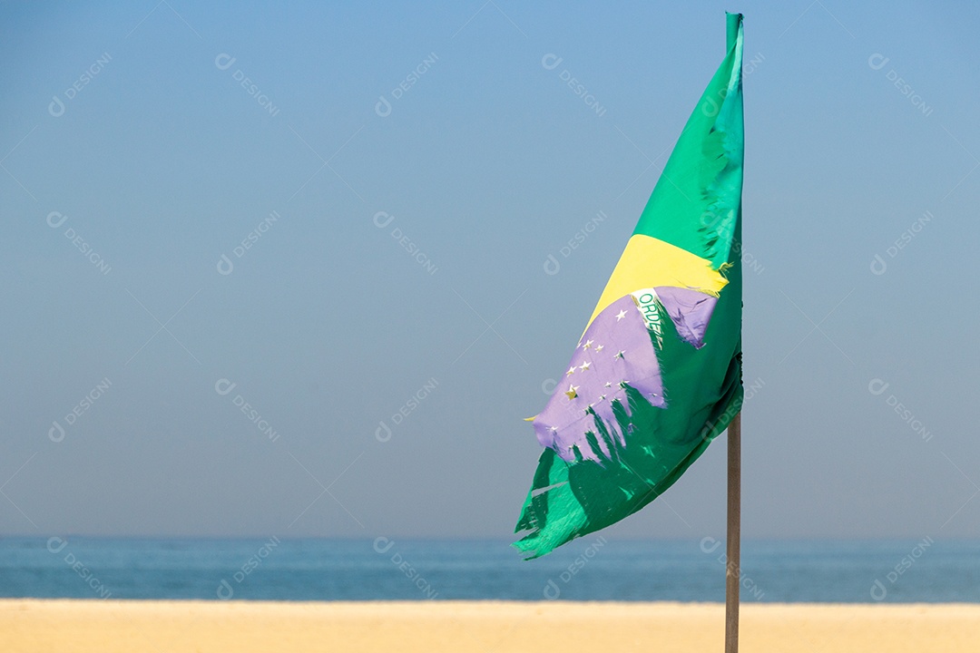 Bandeira do Brasil desbotada e rasgada ao ar livre na praia de Copacabana, no Rio de Janeiro.