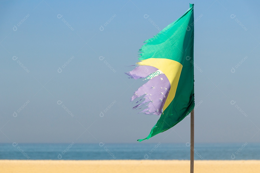 Bandeira do Brasil desbotada e rasgada ao ar livre na praia de Copacabana, no Rio de Janeiro.