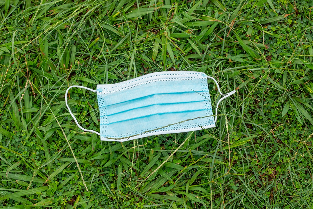 máscara protetora descartável azul, usada para proteção contra o cornavírus, jogada na grama verde do Rio de Janeiro.