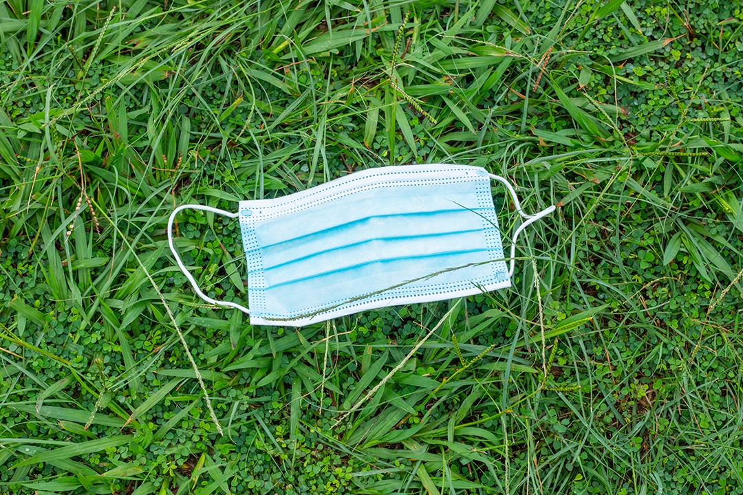 máscara protetora descartável azul, usada para proteção contra o cornavírus, jogada na grama verde do Rio de Janeiro.