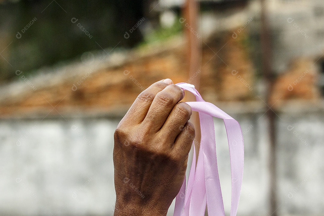 mão de uma mulher negra segurando uma fita rosa fazendo champanhe para a prevenção do câncer de mama no rio de janeiro Brasil.