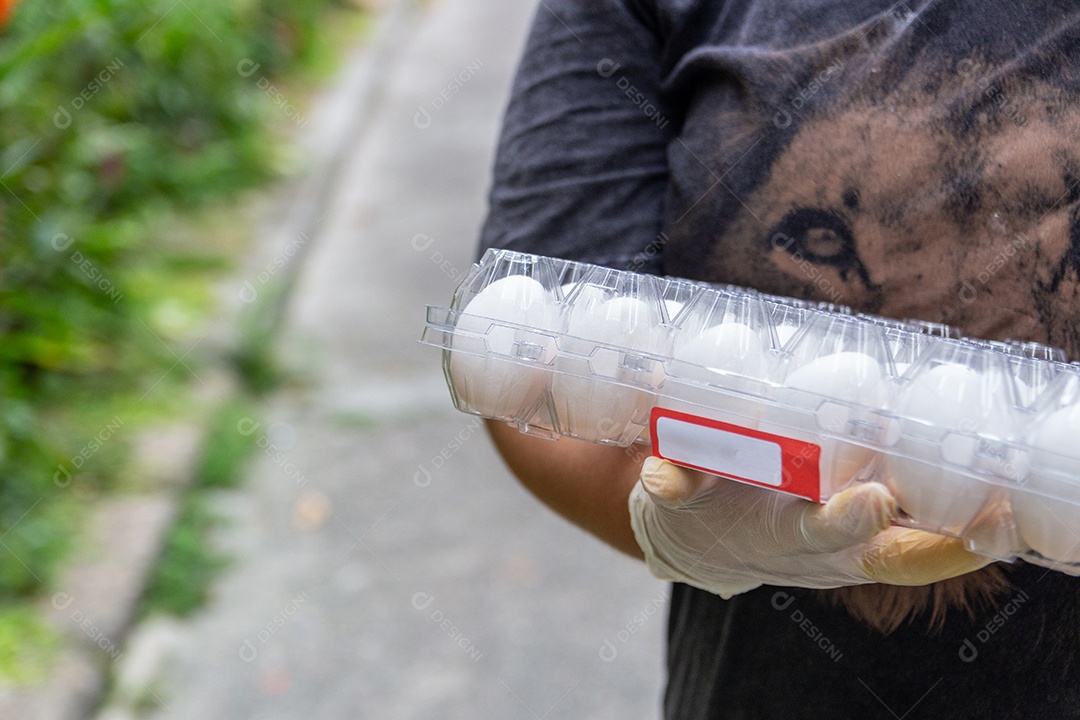 mulher branca segurando caixa de ovos com luva para se proteger do coronavírus no Rio de Janeiro.