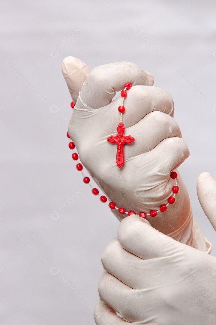 mãos enluvadas brancas segurando um terço vermelho, proteção contra coronavírus no Brasil.