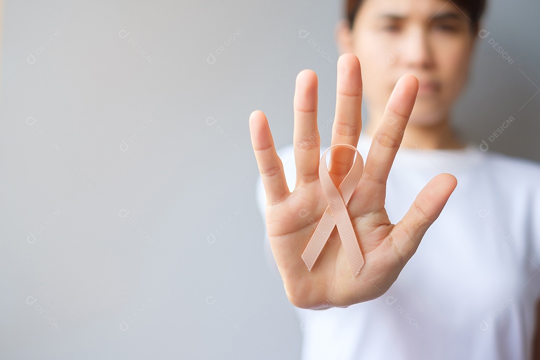 Mão de uma mulher segurando a fita de pêssego para o mês de conscientização do câncer uterino de setembro. Conceito de saúde e dia mundial do câncer