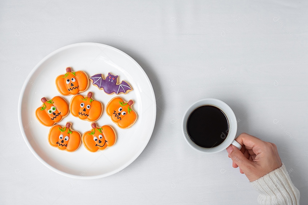 Mão de uma mulher segurando a xícara de café durante comer biscoitos engraçados de Halloween. Feliz dia de Halloween, truque ou ameaça, Olá outubro, outono outono, tradicional, festa e conceito de férias