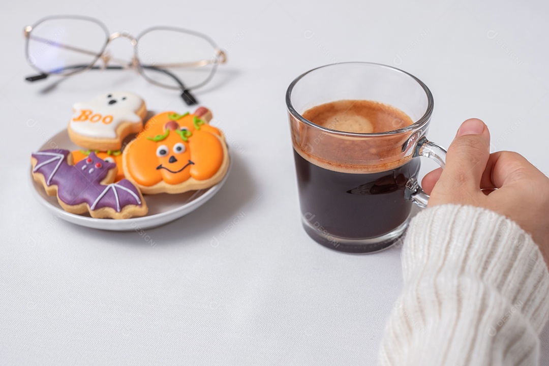 Mão de uma mulher segurando a xícara de café durante comer biscoitos engraçados de Halloween. Feliz dia de Halloween, truque ou ameaça, Olá outubro, outono outono, tradicional, festa e conceito de férias