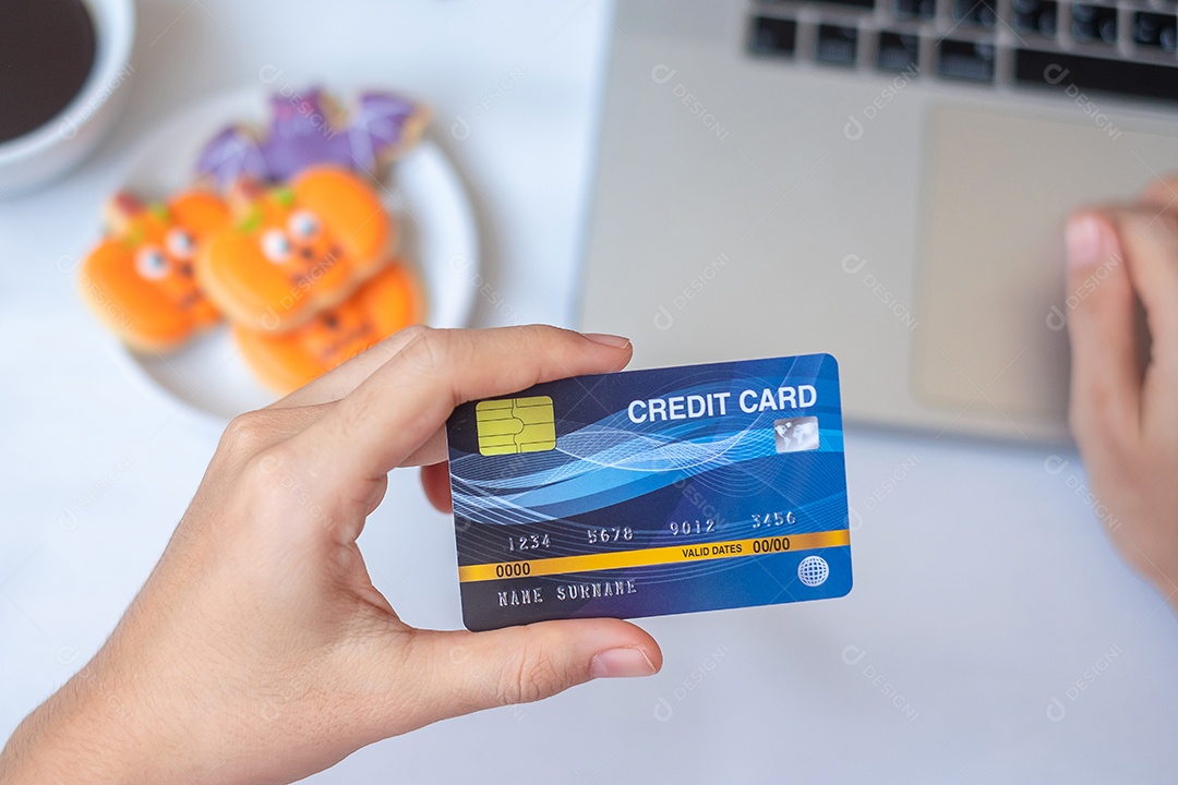 Mão segurando o cartão de crédito para compras on-line no laptop durante a ingestão de biscoitos e café de Halloween. Feliz dia das bruxas, Olá outubro, outono outono, festivo, festa e conceito de férias