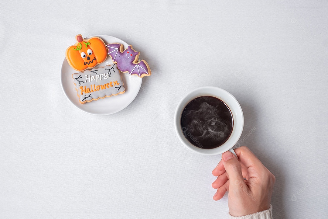 Mão de uma mulher segurando a xícara de café durante comer biscoitos engraçados de Halloween. Feliz dia de Halloween, truque ou ameaça, Olá outubro, outono outono, tradicional, festa e conceito de férias