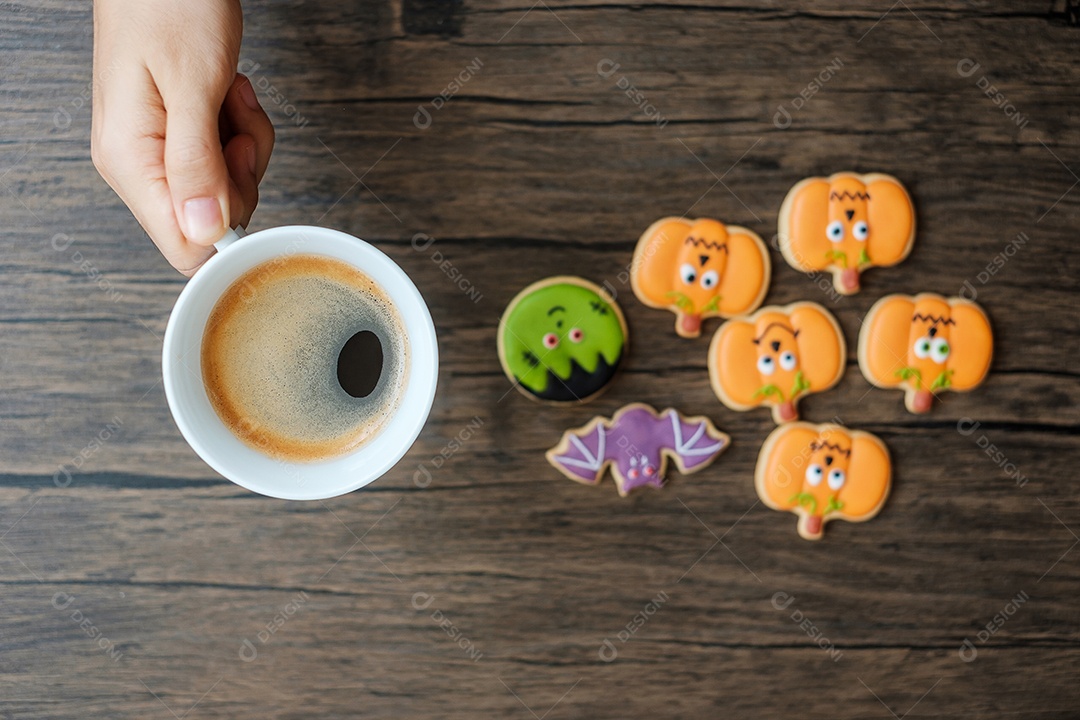 Mão segurando a xícara de café durante comer biscoitos engraçados de Halloween.