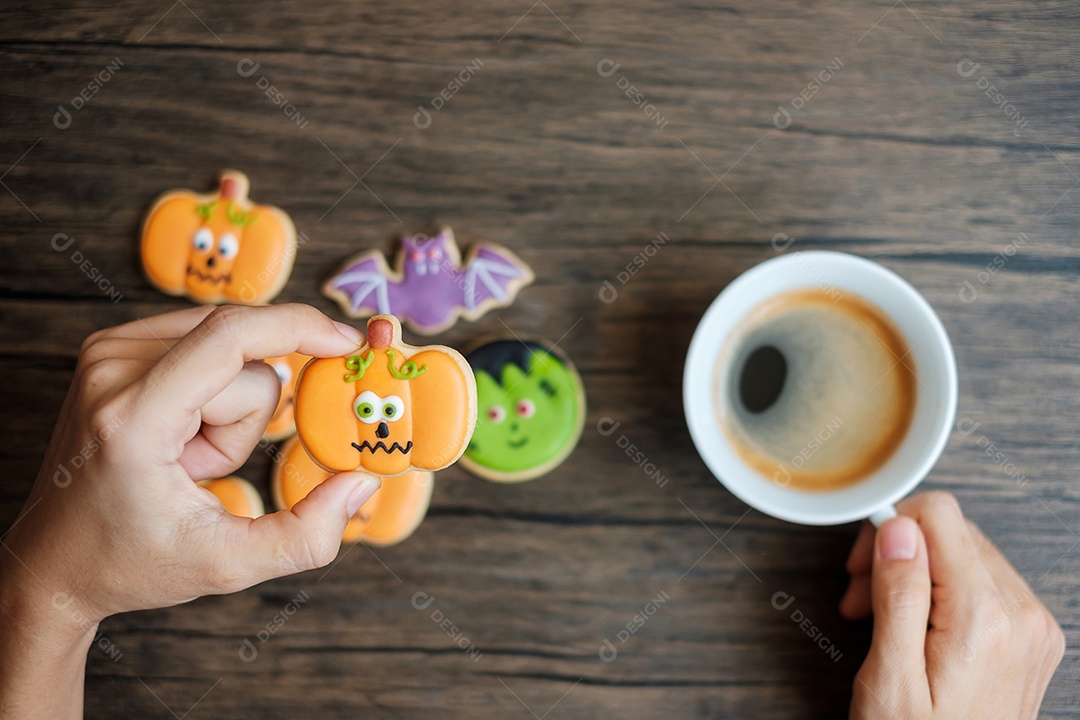 Mão segurando a xícara de café durante comer biscoitos engraçados de Halloween. Feliz dia de Halloween, truque ou ameaça, Olá outubro, outono outono, tradicional, festa e conceito de férias