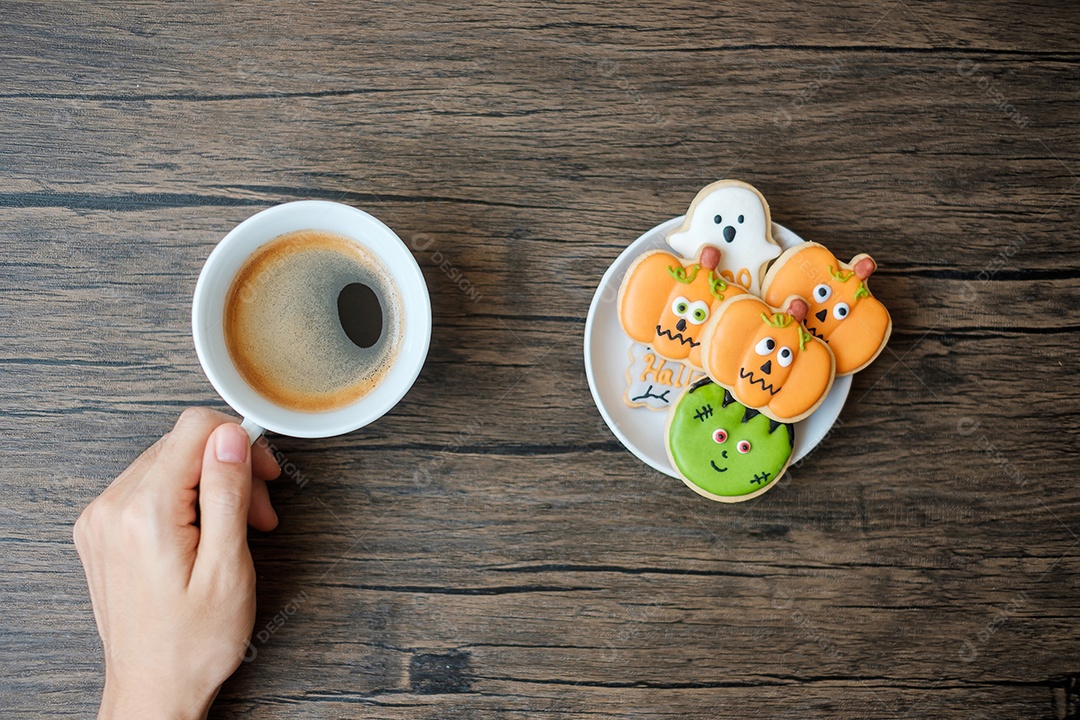 Mão segurando a xícara de café durante comer biscoitos engraçados de Halloween. Feliz dia de Halloween, truque ou ameaça, Olá outubro, outono outono, tradicional, festa e conceito de férias