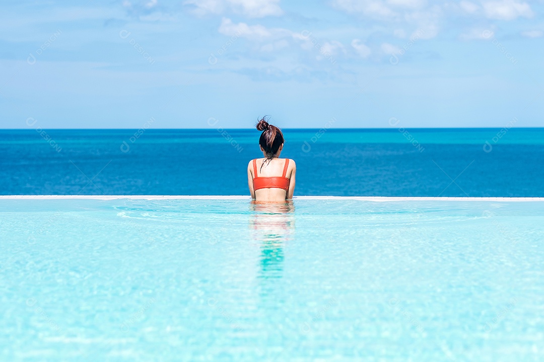 Mulher feliz em maiô laranja nadando na piscina infinita no luxuoso hotel.