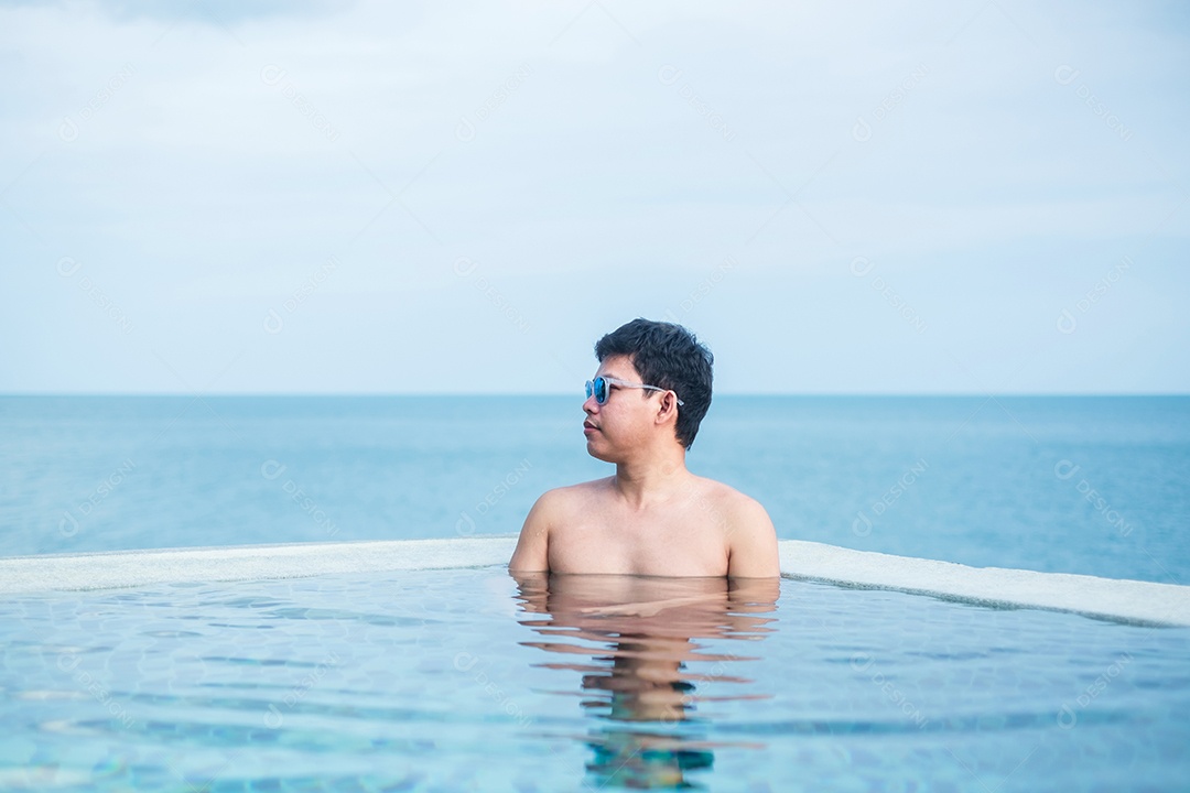 Homem feliz na piscina infinita no hotel de luxo contra o mar.