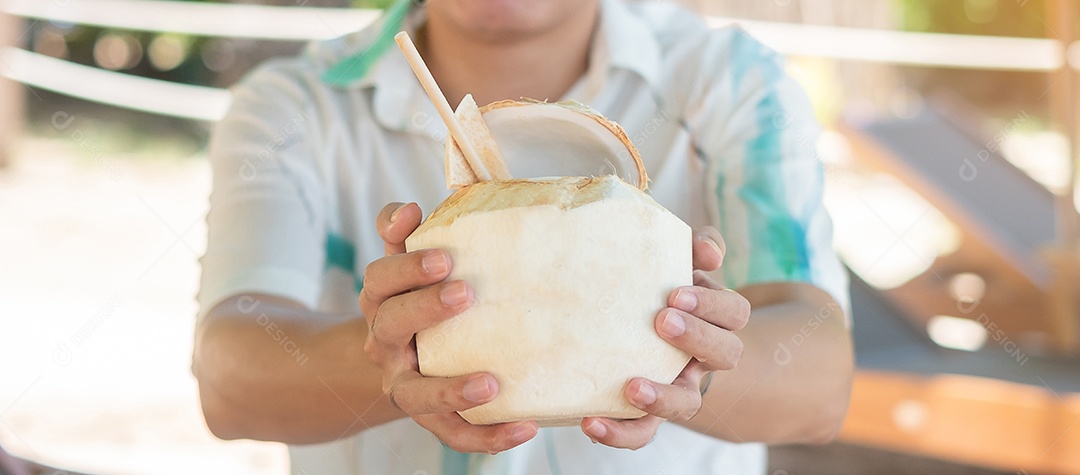 Homem segurando suco de coco fresco durante a bebida na praia tropical.