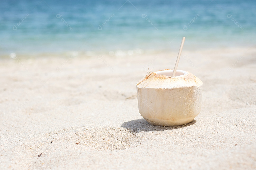 Suco de coco fresco e palha na areia branca contra a praia tropical.