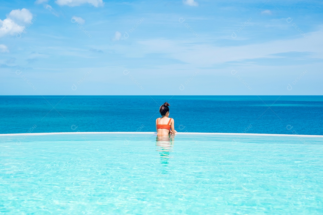 Mulher feliz em maiô laranja nadando na piscina infinita no luxuoso hotel.