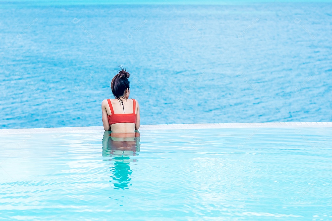 Mulher feliz em maiô laranja nadando na piscina infinita.