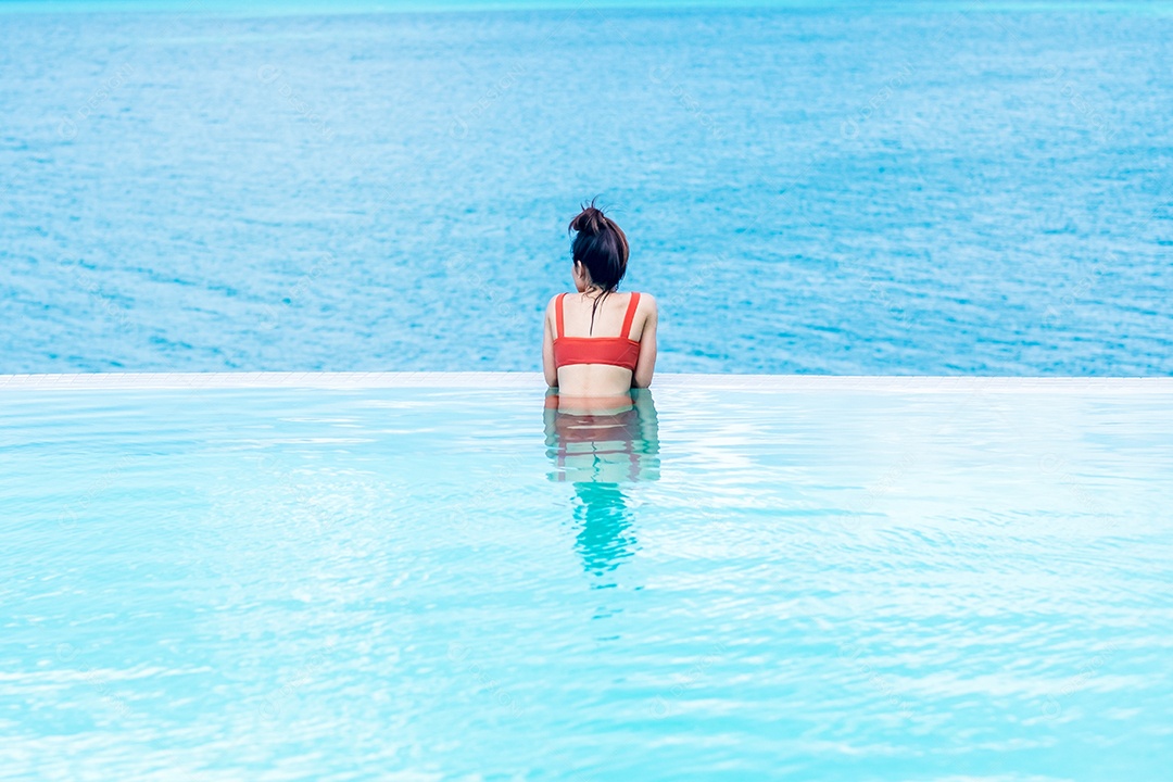 Mulher feliz em maiô laranja nadando na piscina infinita.