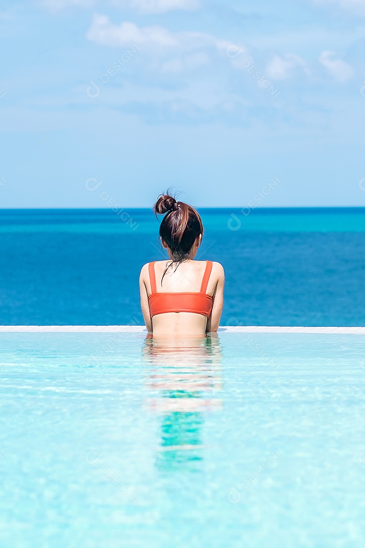 Mulher feliz em maiô laranja nadando na piscina infinita.