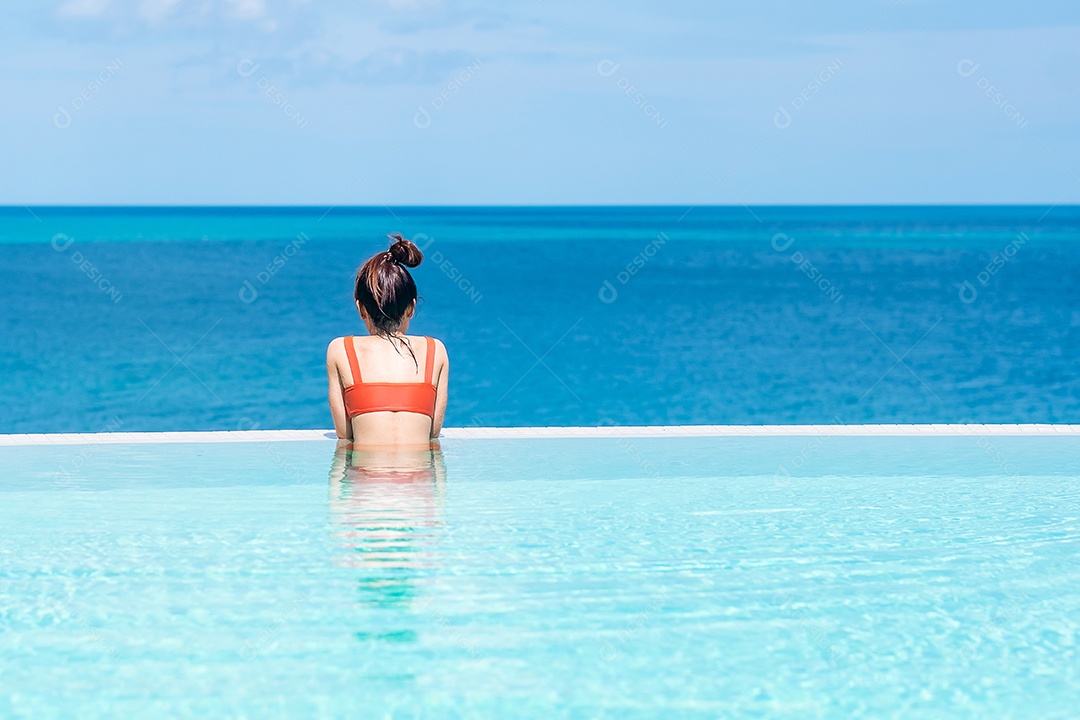 Mulher feliz em maiô laranja nadando na piscina infinita no luxuoso hotel.