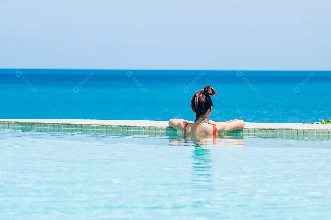 Mulher feliz em maiô laranja nadando na piscina infinita no luxuoso hotel.