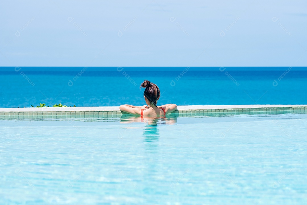 Mulher feliz em maiô laranja nadando na piscina infinita no luxuoso hotel.