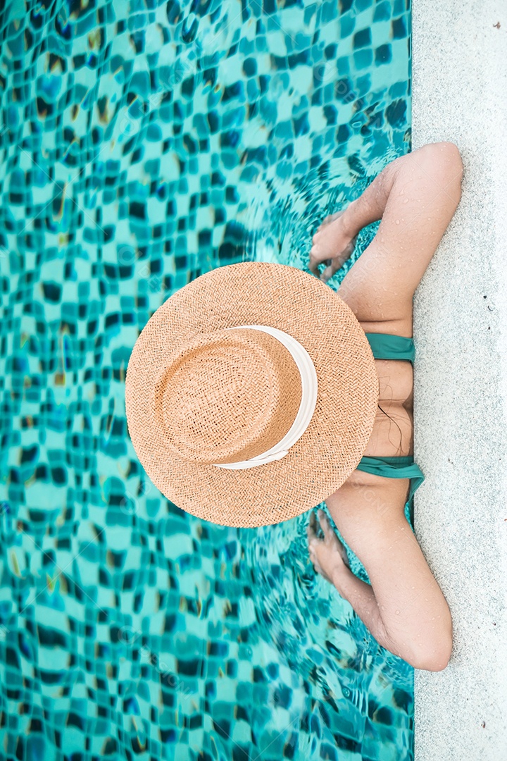 Mulher feliz em traje de banho verde e chapéu na piscina de luxo.