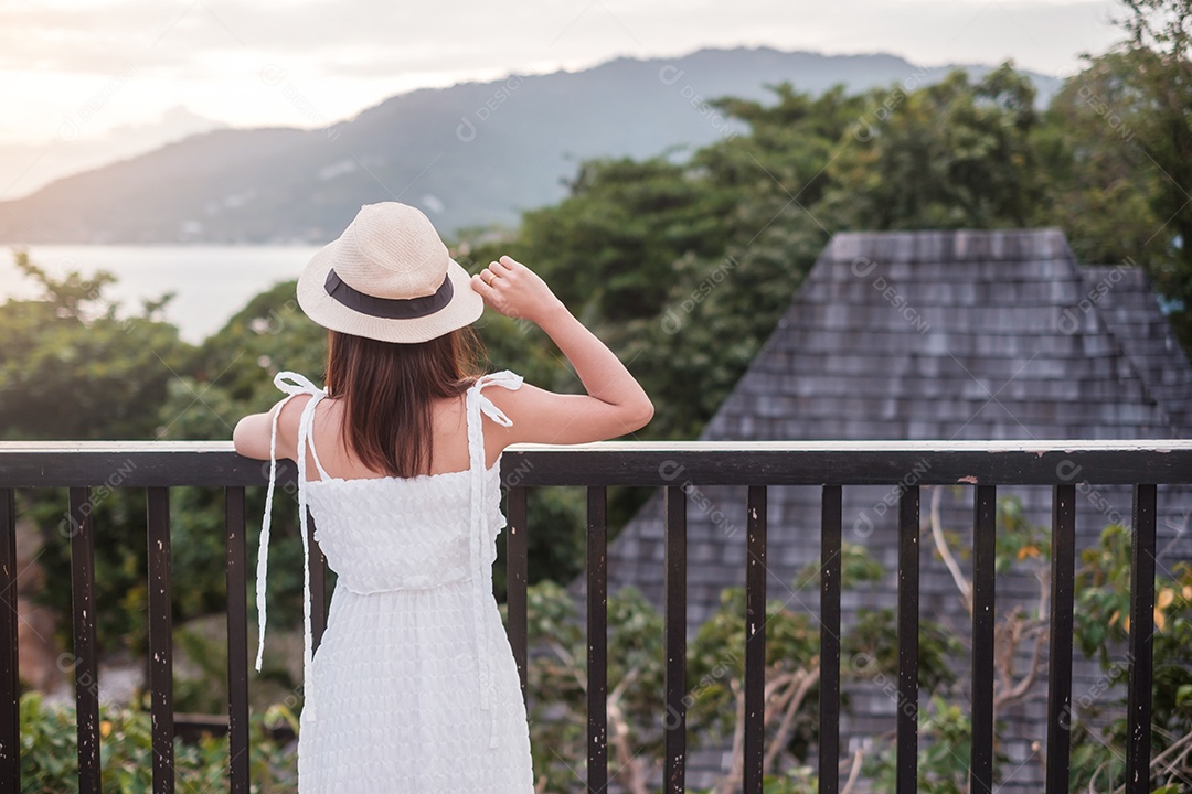 Feliz viajante de vestido branco e chapéu desfruta de um belo mar.