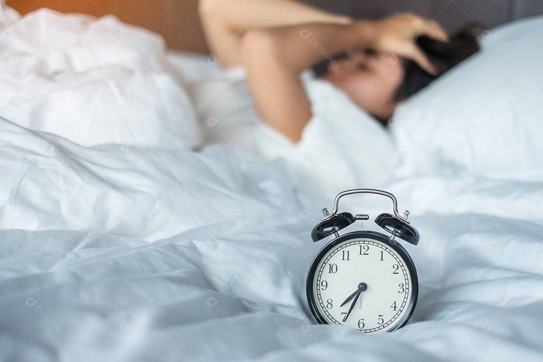 Mulher asiática deitada na cama de manhã com despertador retrô.