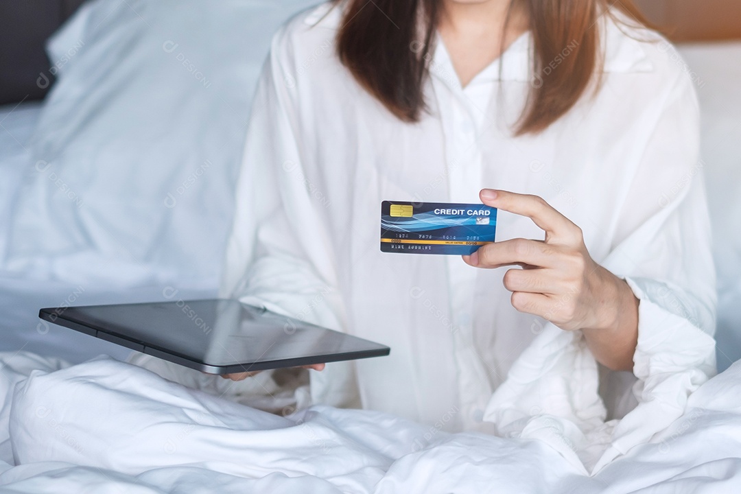 Woman using tablet and credit card for online shopping while ordering in bed in the morning at home.