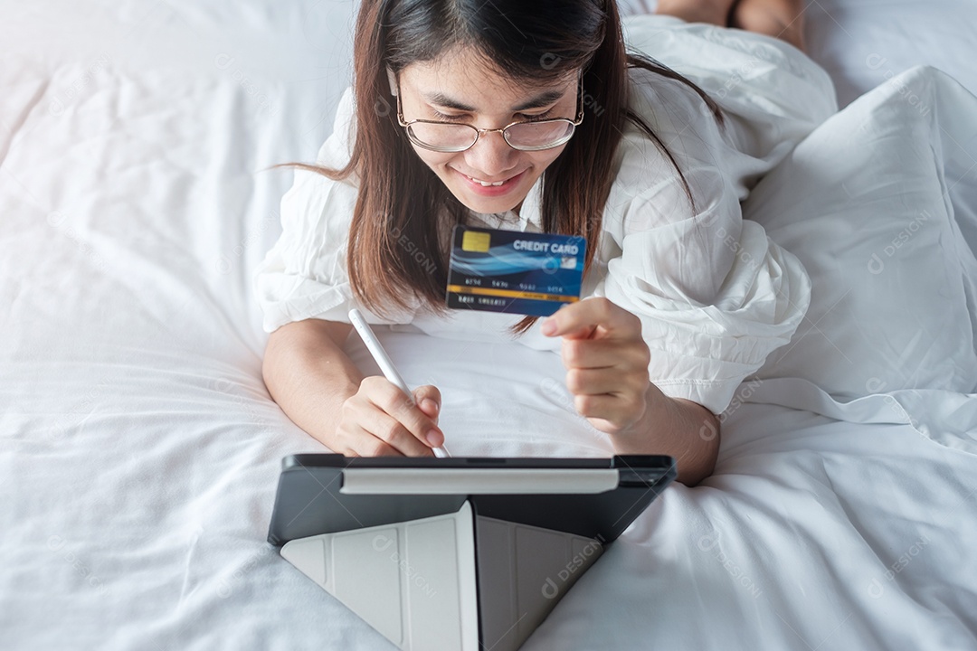 Mulher usando tablet e cartão de crédito para compras online enquanto faz o pedido na cama de manhã em casa.