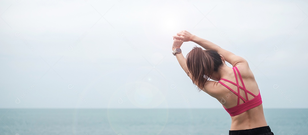 Fêmea jovem fitness em roupas esportivas esticando o corpo contra o oceano.