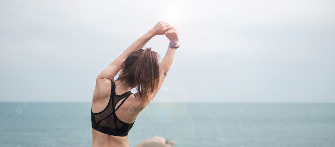 Fêmea jovem fitness em roupas esportivas esticando o corpo contra o oceano.