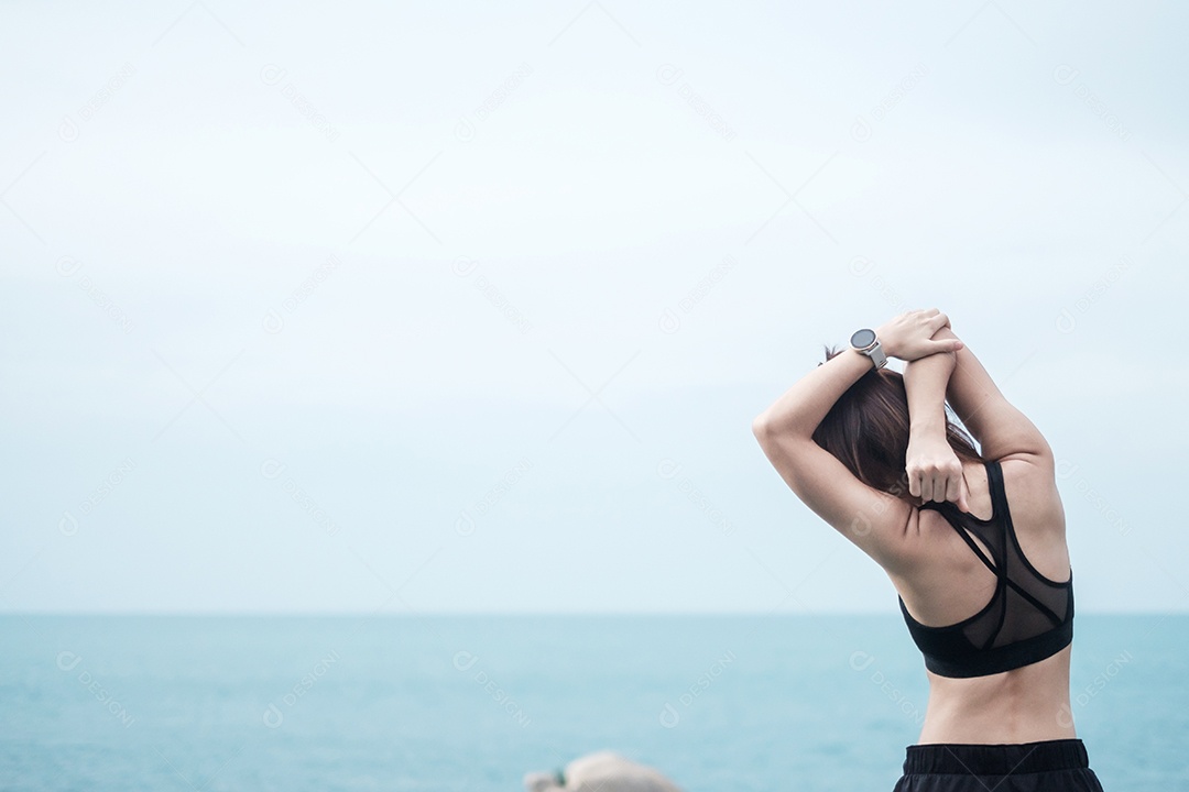 Fêmea jovem fitness em roupas esportivas esticando o corpo contra o oceano.
